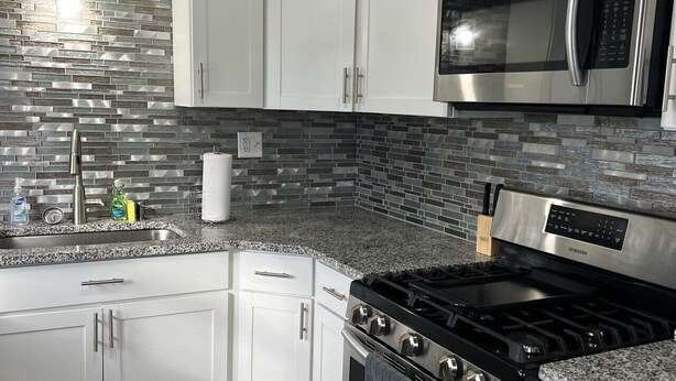 A modern kitchen with white cabinets, a stainless steel microwave, a gas stove, and a tiled backsplash. - GOTL Coastal Cottage- Sunset Vacation Rentals (Geneva)
