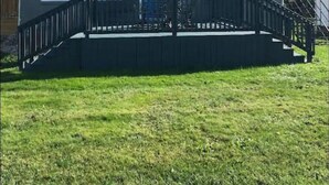 A two-story house with a dark gray exterior, white trim, and blue shutters. There is a covered front porch with a black railing, and a flag is displayed on the door. - GOTL Coastal Cottage- Sunset Vacation Rentals (Geneva)