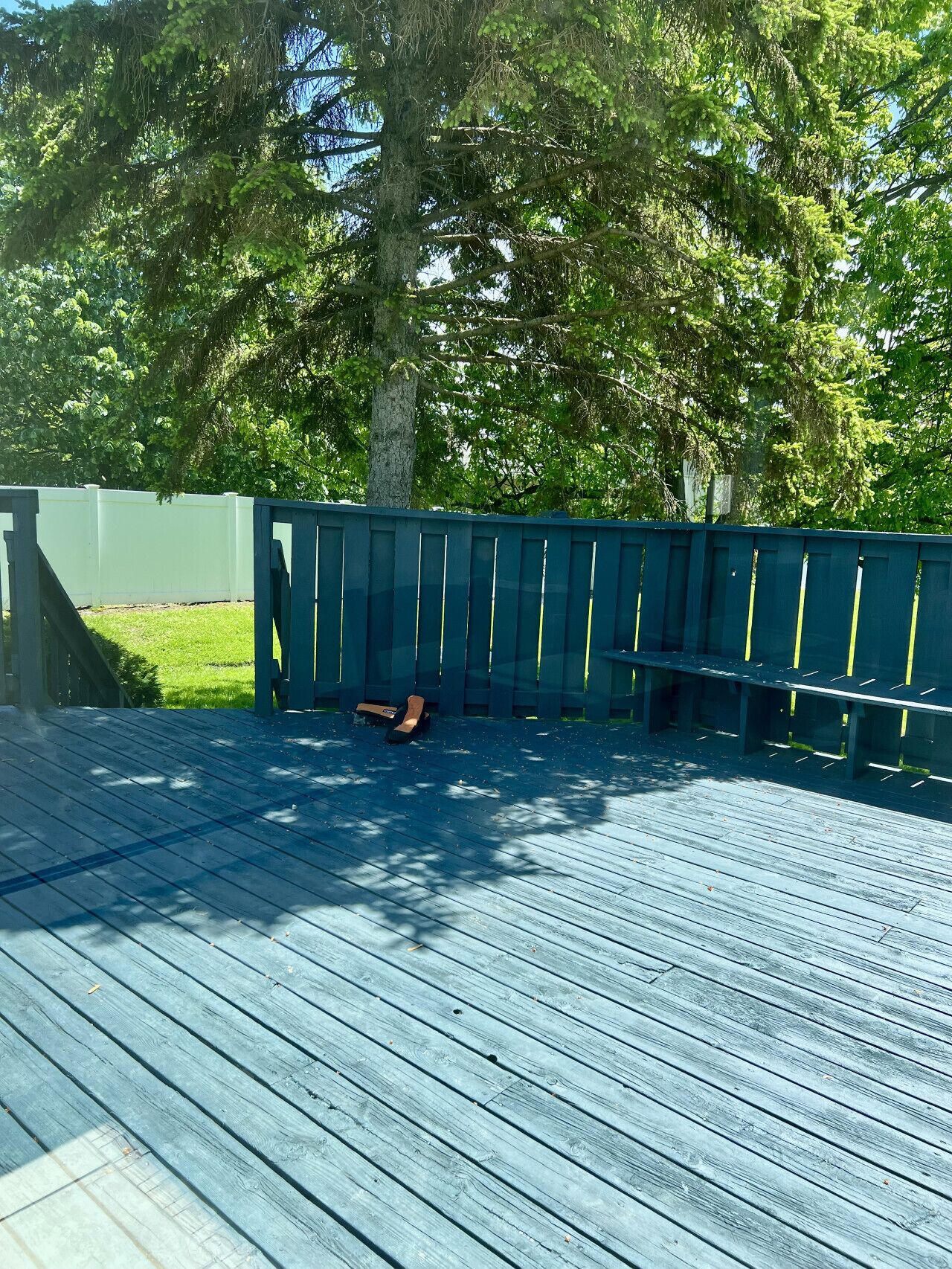 Une terrasse en bois avec une rambarde bleue, entourée d’arbres et d’une clôture blanche.