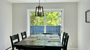 A dining room with a large table, chairs, a hanging light fixture, and a view of a blue fence and greenery outside. - GOTL Winery Mansion- Sunset Vacation Rentals (Geneva)