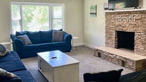 A living room with a stone fireplace, a blue sofa, and a television mounted above it. - GOTL Winery Mansion- Sunset Vacation Rentals (Geneva)