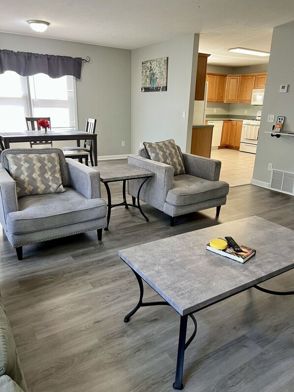 A living room with two grey armchairs, a coffee table, and a dining area with a table and chairs.
