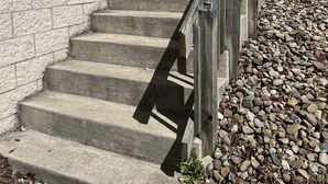 A concrete staircase with a wooden handrail leading to a building with white siding and a stone foundation. - Seascape Townhome #69- Sunset Vacation Rentals (Geneva)
