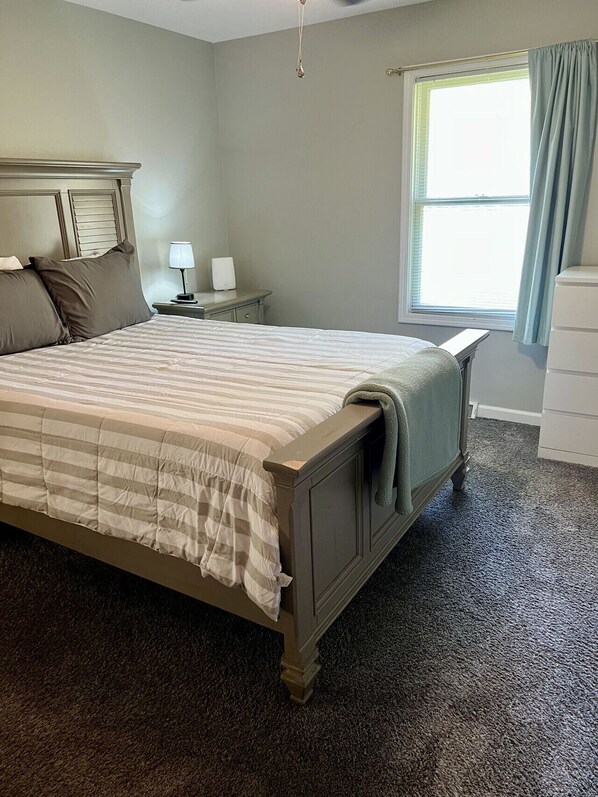 A bedroom with a bed, nightstand, lamp, and window with curtains.