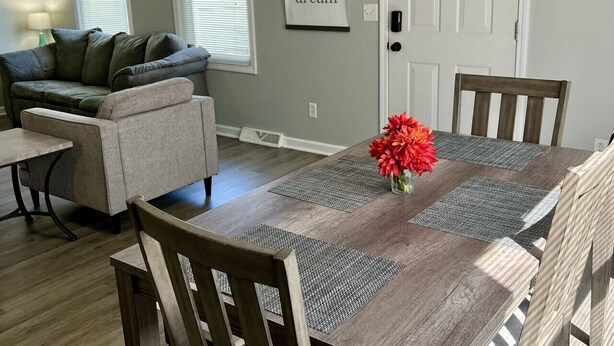 A dining area with a wooden table and chairs, a sofa, and a wall with a motivational quote. - Seascape Townhome #69- Sunset Vacation Rentals (Geneva)