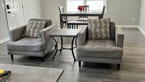 A living room with two grey armchairs, a coffee table, and a dining table with chairs. - Seascape Townhome #69- Sunset Vacation Rentals (Geneva)