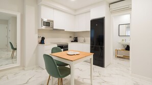 A compact kitchen with white cabinets, a microwave, a coffee maker, and a black refrigerator. There is a dining table with two chairs. - Loft Estudio near Las Canteras beach (Las Palmas de Gran Canaria)