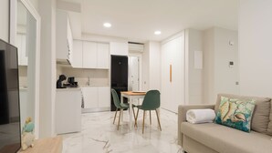 A modern living room with a sofa, a dining table with chairs, a kitchen area with cabinets, and a TV. - Loft Estudio near Las Canteras beach (Las Palmas de Gran Canaria)