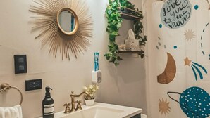 A bathroom with a vanity, sink, and toilet. There is a mirror with a sunburst design, a shower curtain with a space-themed design, and a small plant on a shelf.
