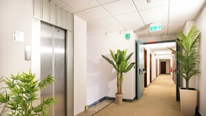 A hotel corridor with an elevator, potted plants, and a sign indicating an exit. - Camelia Rooms Venice Guesthouse near Mestre Train Station - 24 rooms (Venezia)