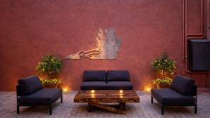 An outdoor seating area with two sofas and a wooden coffee table, flanked by potted plants, against a textured wall with a decorative metal piece. - Camelia Rooms Venice Guesthouse near Mestre Train Station - 24 rooms (Venezia)