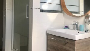 A bathroom with a glass shower enclosure, a vanity with a mirror, and a sink. - Le Saint Merry apartment in Fontainebleau in a quiet, central location. (Fontainebleau)