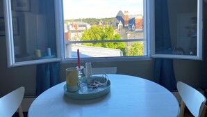 A round table with a metal tray, a mug, and a candle. A window with a view of buildings and trees is in the background. - Le Saint Merry apartment in Fontainebleau in a quiet, central location. (Fontainebleau)