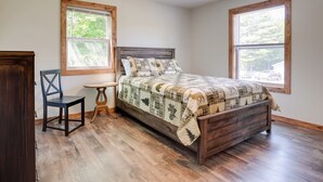 Una camera da letto con un letto in legno, due finestre, una sedia e un tavolino.