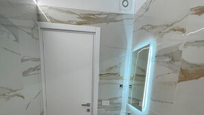 Um banheiro moderno com parede de mármore, pia branca e espelho iluminado por LED.