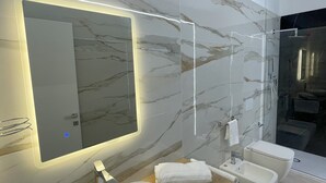 Casa de banho moderna com painel de parede de mármore, um espelho grande, uma pia, um bidé e cabine de duche em vidro.