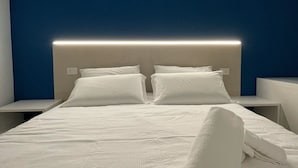 Cama bem arrumada com lençóis brancos, duas almofadas e uma toalha dobrada ao lado.