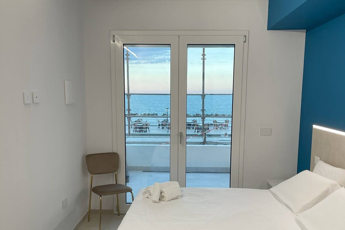 Une chambre à coucher avec un lit, une chaise et une vue sur la mer, visible à travers une porte vitrée.