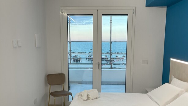 Quarto com uma cama, uma cadeira e vista para o mar através de uma porta de vidro.
