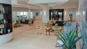 Um hall amplo com design moderno, apresentando uma área de estar com sofás e poltronas, um balcão de recepção e uma grande parede espelhada.