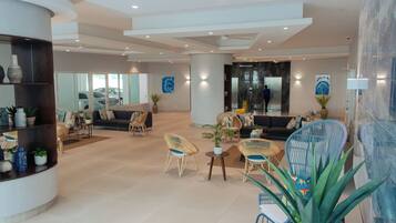 A spacious lobby with a modern design, featuring a seating area with sofas and chairs, a reception desk, and a large mirror wall.