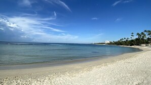 Uma praia com águas azul-claras, areal arenoso e palmeiras.