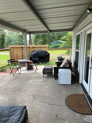 A covered patio with a table and chairs, a grill, and a wicker chair.
