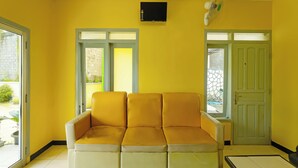 Una habitación con pared amarilla, techo blanco, sofá amarillo y puerta verde.