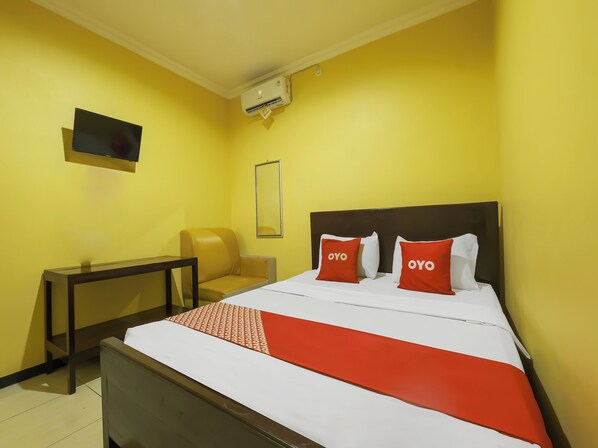 A hotel room with a bed, a chair, a TV, and an air conditioning unit.