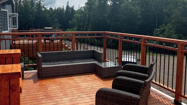 Una terraza de madera con mobiliario de mimbre, un banco de madera y una barandilla.