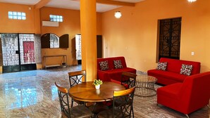 A spacious room with a high ceiling, a central wooden dining table surrounded by chairs, and two red sofas with patterned cushions. - Hotel y Restaurante La Perla (Cacaopera)