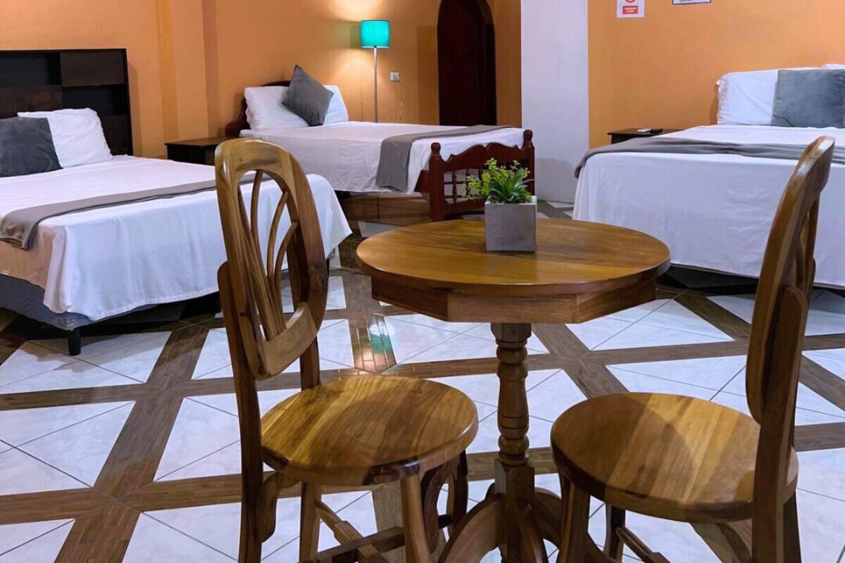 A hotel room with two beds, a round wooden table, and two wooden chairs.
