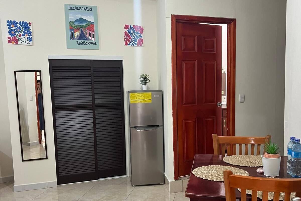 A dining area with a table and chairs, a refrigerator, a door, and a mirror.