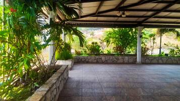 Una zona patio coperta con pareti in pietra e pavimento piastrellato, immersa nel verde e con vista su un paesaggio collinare.