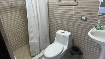 Un baño con inodoro, cortina de ducha, lavabo y cubo de basura.