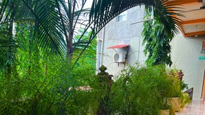 A corridor with potted plants, marble flooring, and a building with a red awning in the background. - Hotel y Restaurante La Perla (Cacaopera)