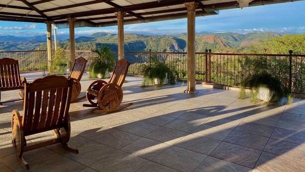 A covered terrace with wooden chairs, a view of mountains, and a tiled floor. - Hotel y Restaurante La Perla (Cacaopera)