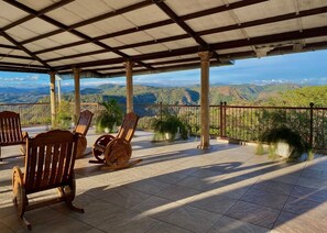 A covered terrace with wooden chairs, a view of mountains, and a tiled floor. - Hotel y Restaurante La Perla (Cacaopera)