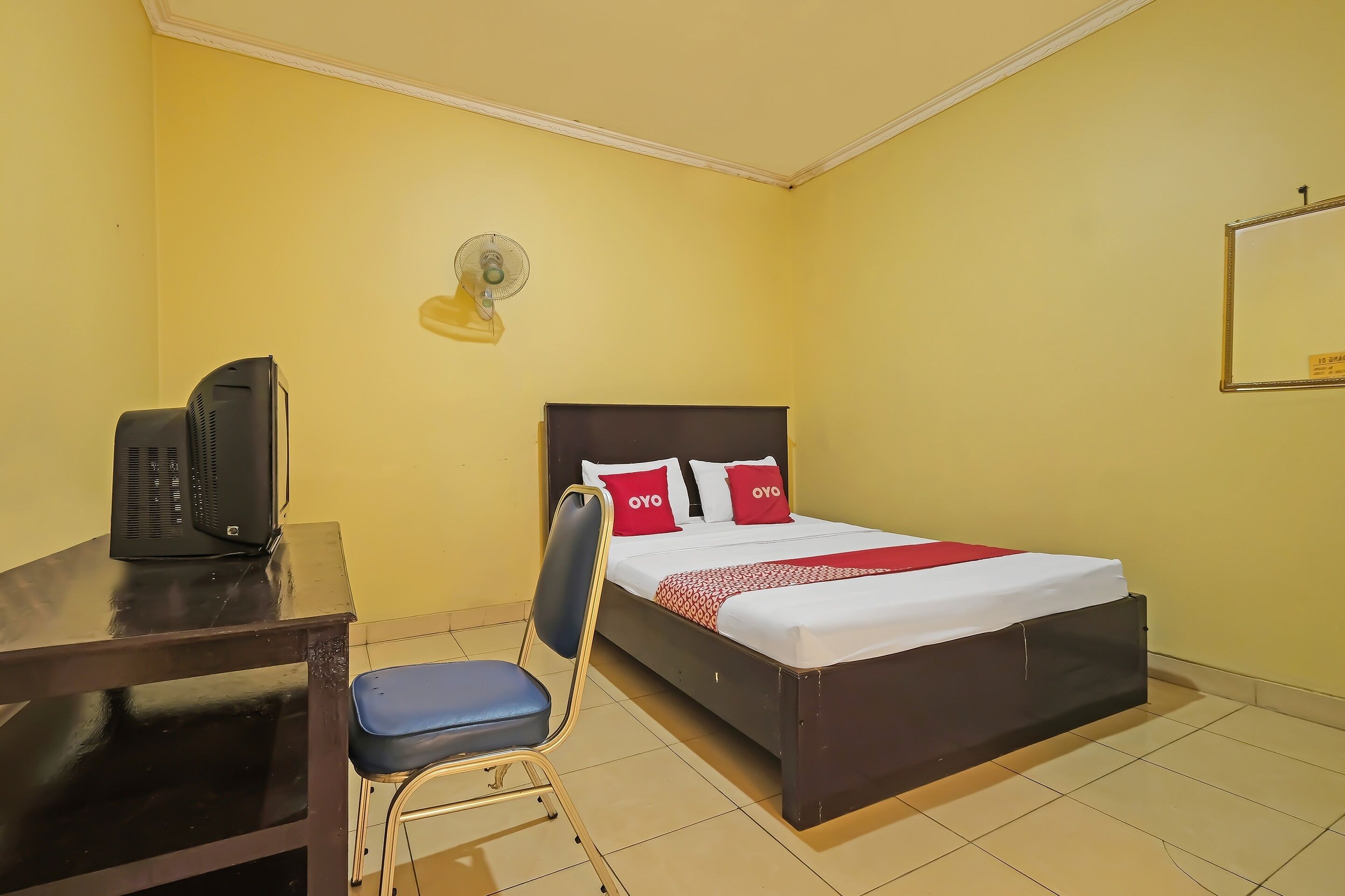 Une chambre d’hôtel équipée d’un lit, d’un bureau avec un téléphone, d’une chaise et d’un ventilateur fixé au mur.