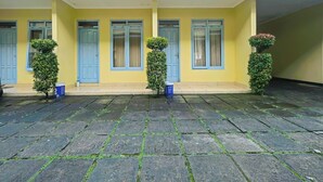 Un bâtiment jaune avec des portes et des fenêtres bleues, un toit recouvert de tuiles et des plantes en pot.