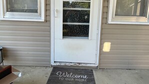 A front door with a welcome mat, two windows with blinds, and a concrete driveway. - Nana's Townhouse centrally located in the Heart of the Ozarks.  (Licking)