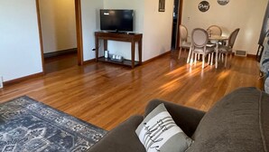 A living room with a TV on a wooden stand, a gray sofa, a patterned rug, and a dining area with a table and chairs. - Nana's Townhouse centrally located in the Heart of the Ozarks.  (Licking)