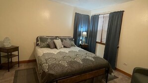 A bedroom with a bed, a ceiling fan, a nightstand, a lamp, and a window with curtains. - Nana's Townhouse centrally located in the Heart of the Ozarks.  (Licking)