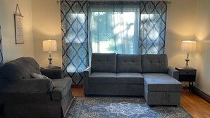 A living room with a grey sectional sofa, a grey armchair, two side tables with lamps, and a patterned rug on a wooden floor. - Nana's Townhouse centrally located in the Heart of the Ozarks.  (Licking)