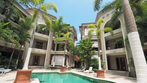 A pool area with a clear blue pool, surrounded by palm trees and lounge chairs. - Family Paradise Macaws 3 (Jacó)