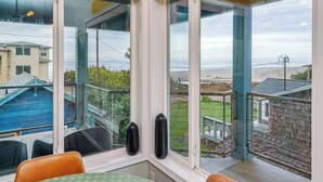 Habitación con un amplio ventanal con vistas a la playa y a una piscina. Hay dos objetos cilíndricos negros en el alféizar.