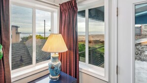 Una habitación con vistas al mar a través de amplios ventanales, una mesa con una lámpara y una cortina.