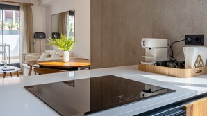 A modern hotel room with a kitchen area, a dining table with a vase of green plants, a coffee machine, and a large mirror on the wall. - GA1 (Barcelona)