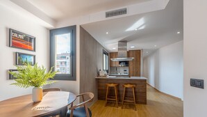A modern kitchen with wooden cabinets, a central island with stools, and a dining area with a table and chairs. - GA1 (Barcelona)