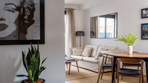 A modern living room with a sofa, a dining table with chairs, a potted plant, and a large mirror on the wall. - GA1 (Barcelona)